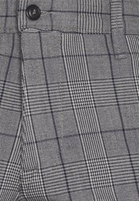 Grå och marinblå rutigt tyg med en blandning av hundtandsmönster och rutig design, med en slät textur och en knappdetalj i midjan.