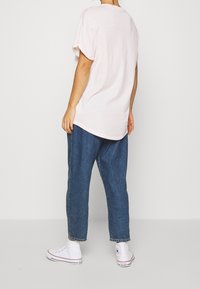 Jasnoróżowa bawełniana koszulka o luźnym kroju, z krótkimi rękawami i okrągłym dekoltem, w zestawie z luźnymi, ciemnoniebieskimi dżinsami i białymi trampkami.