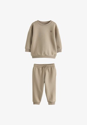 Beige langærmet sweatshirt med lille smilende ansigtsdetalje kombineret med matchende bukser med elastisk talje og snøre til børn.