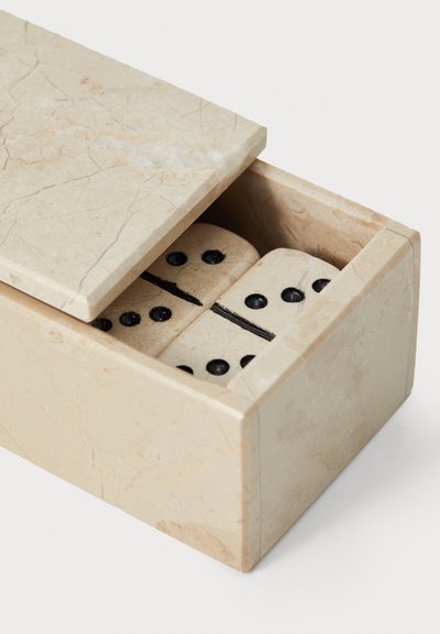 Juego de dominó en una caja de mármol beige claro, con puntos negros en piezas rectangulares. La caja tiene un acabado suave con costuras mínimas visibles.