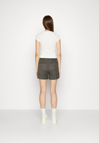 T-shirt bianca aderente a maniche corte abbinata a pantaloni corti a quadri marroni. I pantaloni corti hanno tasche laterali e una vita elastica. Sneakers bianche.