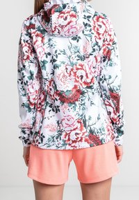 Sudadera con capucha floral en blanco con flores rosas y verdes. Combinada con pantalones cortos de color coral. Presenta mangas largas y capucha con cordón.
