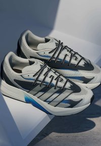 Sive i crne tenisice za trčanje izrađene od mrežastih i sintetičkih materijala, s elegantnim dizajnom, crnim vezicama i plavim detaljima na potplatu.