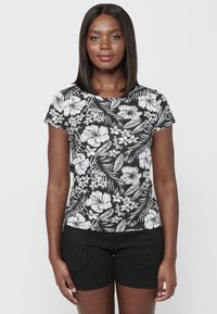 Juoda trumpa rankovė t-shirt su kontrastiniu balto gėlių raštu, apvaliu kaklu ir švelnia medžiaga. Sujungta su juodomis šortais.