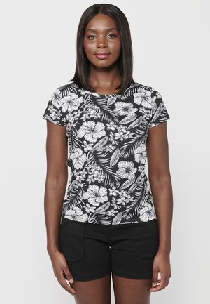 T-shirt noir à manches courtes avec un motif floral blanc contrastant, col rond et tissu doux. Associé à un short noir.