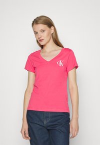Camiseta de algodón rosa con diseño de escote en forma de V y mangas cortas, con un pequeño logo blanco en la parte izquierda del pecho.