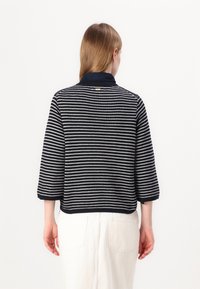 Pulover cu dungi bleu marin și crem, cu mâneci până la cot și guler. Textură tricotată, croială scurtă și un detaliu cu etichetă pe spate vizibil.