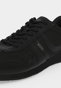 Baskets noires à lacets avec panneaux latéraux texturés et logo "BOSS" sur le côté extérieur, dotées d'une semelle en caoutchouc à profil bas.