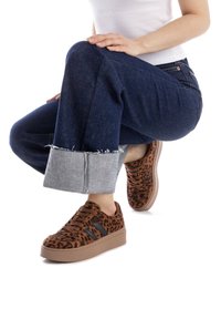 Zapatillas de deporte con estampado de leopardo marrón, con un upper texturizado, rayas negras y una suela gruesa beige, combinadas con unos vaqueros oscuros de mezclilla enrollados.