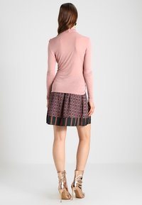 Långärmad rosa topp som matchas med ett mönstrat kjol med mörka och färgglada ränder. Outfitten kompletteras av glänsande metalliska ankelstövlar.