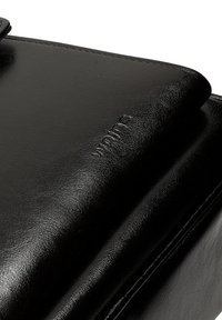 Černá kožená taška s hladkým povrchem, s decentně vyraženým logem. Design se sklápěcí klopou s čistými okraji a minimálním kovovým příslušenstvím.