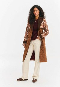 Brązowy pikowany płaszcz trencz z wzorem w kropki, z dużym kołnierzem, dwurzędowymi guzikami i gładkim wykończeniem materiału.