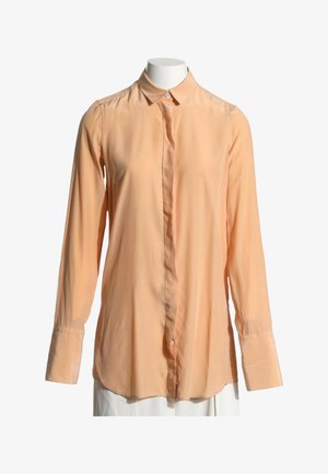 Langærmet ferskenfarvet skjorte med knapper og spids krave på en hvid mannequin overkrop mod en hvid baggrund.