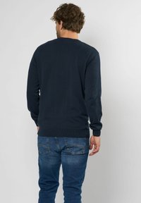 Navyblauwe trui met lange mouwen en een ronde hals, voorzien van geribbelde manchetten en zoom. G gedragen met lichtblauwe spijkerbroek.