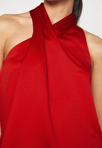 Rød halterneck top med draperet halsudskæring, lavet af glat stof. Har et tætsiddende design og symmetrisk detaljer på skuldrene.