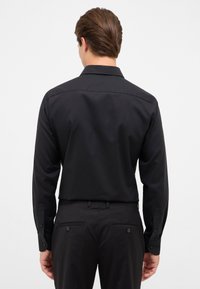 Schwarz, langärmliges Hemd mit geknöpften Manschetten, glatter Textur, dezenter Kragen und taillierte Passform; kombiniert mit schwarzen Hosen mit Gesäßtaschen.