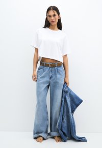 Tricou alb scurt cu mâneci scurte, blugi largi de un bleumarin deschis cu un brâu maro și o jachetă din denim purtată pe un braț.