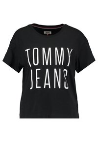 Černé tričko s krátkým rukávem a velkým bílým nápisem "TOMMY JEANS" na přední straně, má kulatý výstřih a štítek značky uvnitř.