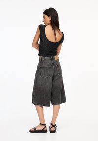 Schwarzes, eng anliegendes Top mit einem tiefen Rückendesign, das mit lockeren, grauen Denim-Culottes kombiniert ist. Die Sandalen haben ein einfaches Riemendesign.
