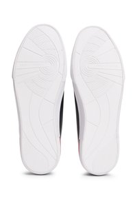 Valkoiset kumipohjat, joissa on kuvioidut pitoalueet, musta sivuosa ja punainen yksityiskohta kannassa, joissa on brändin logo kohokuvioituna.