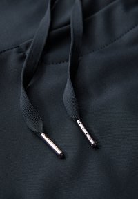 Svart tyg med texturerad yta och två dragsnören. Varje snöre har en metallspets med hål, vilket förbättrar funktionaliteten.