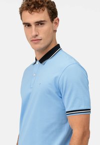 Polo shirt blu chiaro realizzato in tessuto testurizzato, con colletto nero a righe bianche e tre bottoni sul collo.