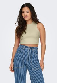 Licht olijfgroen geribbeld cropped top met een hoge hals, gecombineerd met hooggetailleerde blauwe jeans met fijne strepen, zakken en knoopsluiting.