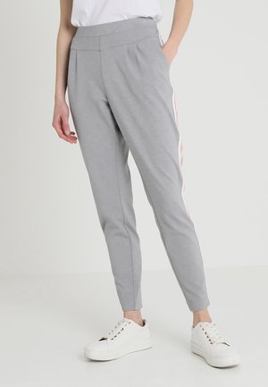 Pantalones grises ajustados con un acabado texturizado, con pierna tipo tapered y franjas laterales en rosa y blanco. Combinados con zapatillas blancas.