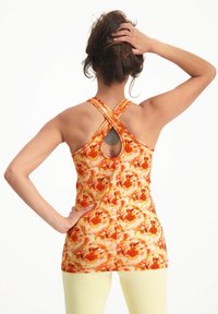 Racerback-topp i en ljus orange och gul batikmönster, med en öppen rygg och cirkulär urtagning. Stretchigt material och åtsittande design.