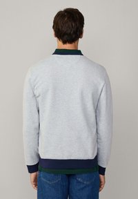 Sudadera gris con cuello azul marino oscuro, puños y dobladillo de canalé. Textura suave, diseño ajustado y estilo casual evidente desde la vista trasera.