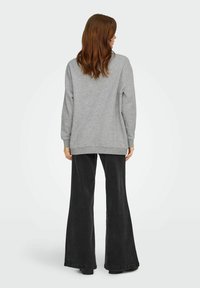 Sudadera gris de manga larga, con puños y dobladillo acanalados; combinada con pantalones negros de campana. Diseño sencillo, tejido suave, corte holgado.