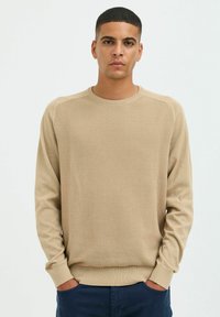 Pull en tricot beige avec une texture côtelée, un col rond et des manches longues. Présente une coupe décontractée et des rayures horizontales.