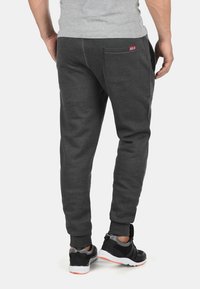 Graue Sweatpants mit einem schmal zulaufenden Design, aus weichem Stoff, ausgestattet mit einer Gesäßtasche und elastischen Bündchen, kombiniert mit schwarzen Sportschuhen.