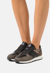 Black and gray sneakers with a mix of smooth and textured materials, featuring laces, a white sole, and subtle branding details.