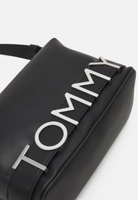 Czarna skórzana torebka o eleganckim prostokątnym kształcie, z dodatkiem srebrnego logo "TOMMY" oraz regulowanym paskiem.