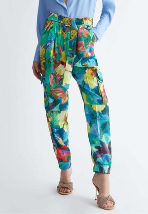 Jasne, kwieciste spodnie z wysokim stanem z paskiem, kieszeniami typu cargo, mankietami u dołu, połączone z niebieską koszulą i beżowymi sandałami na wysokim obcasie.