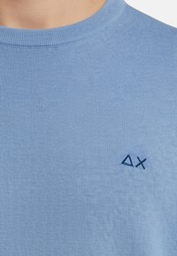 Maglione a girocollo azzurro realizzato in tessuto a coste; presenta un piccolo logo blu scuro sul petto a sinistra. Tessuto morbido, design minimale.