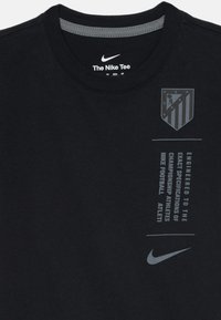 Czarna bawełniana koszulka z okrągłym dekoltem, z szarym logo Atlético Madryt i tekstem na przodzie, oraz brandingiem Nike wewnątrz kołnierza.