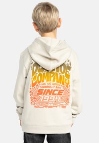 Ljusbeige hoodie med en stor flerfärgad grafisk design på baksidan i orange och gult, med text och mönster. Har en dragsko på huvan och en ficka fram.