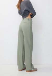 Pantalon vert clair à jambe large avec une texture lisse, doté d'une taille classique et de poches arrière, associé à un pull gris foncé côtelé.