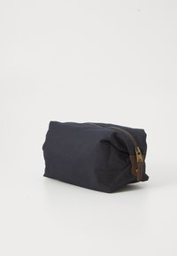 Pocchetto rettangolare blu navy in tessuto con zip in ottone e linguetta in pelle marrone su una superficie bianca semplice.