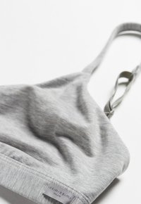 Ljust grå bralette i mjukt tyg med tunna justerbara band och en etikett märkt "Intimissimi" placerad längst ner.