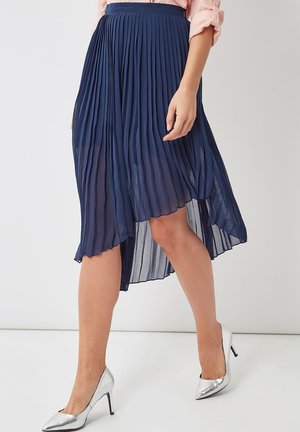Falda midi plisada en color navy con un dobladillo asimétrico, hecha de una tela ligera. Presenta una cintura ajustada y una textura fluida. Tacones plateados visibles.