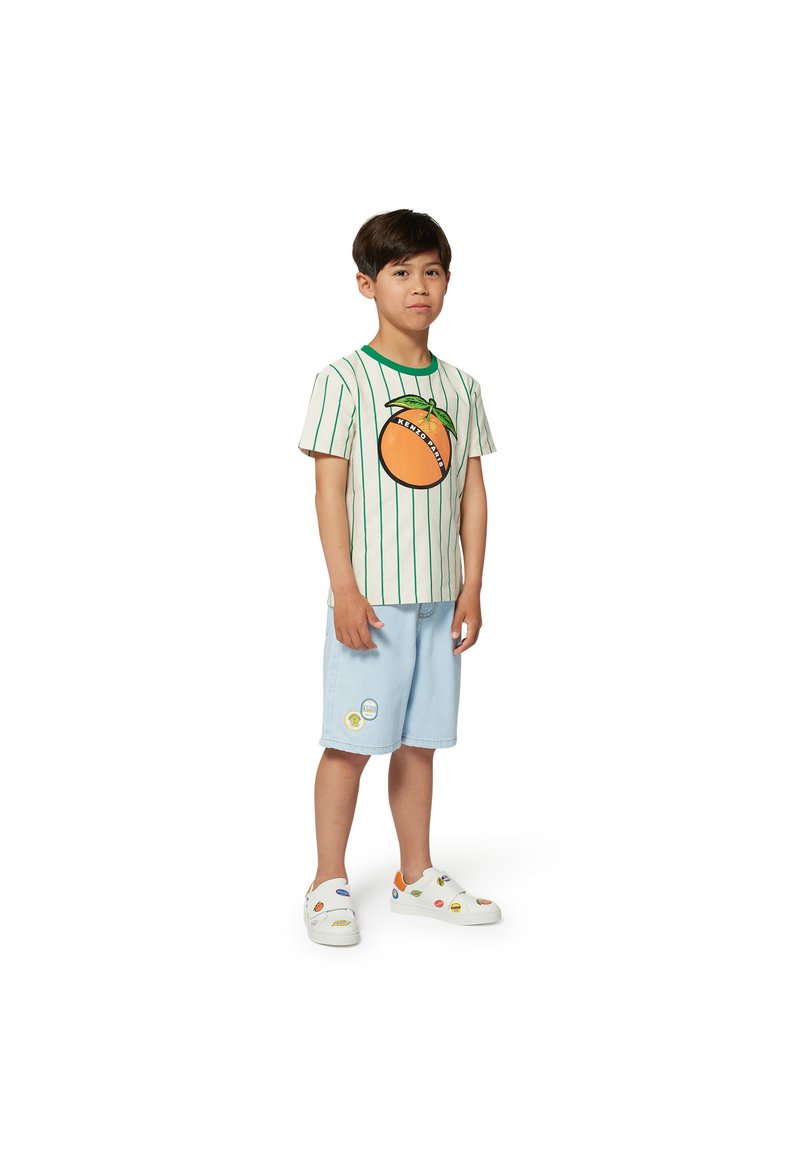 T-shirt à manches courtes rayé avec un motif orange, un col vert, un short bleu clair avec des patchs et des baskets blanches avec des accents colorés.