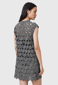 Rochie din croșetat gri, având un design stratificat cu modele circulare, mâneci scurte și margine ondulată. Material cu țesătură deschisă și texturat.