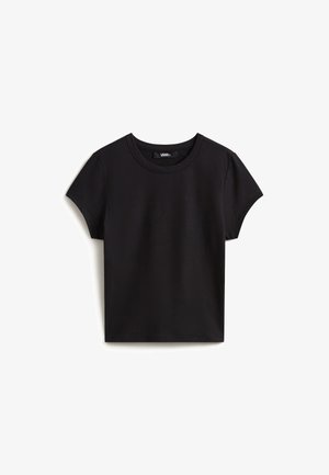 Camiseta negra de manga corta de algodón con cuello redondo y etiqueta del logo Vans dentro del cuello, extendida sobre un fondo blanco.