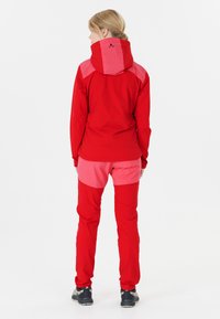 Röd och rosa utomhusjacka med matchande byxor, utrustad med huva, justerbara ärmslut och paneler i kontrasterande färger. Mjuk textur, sportig design.