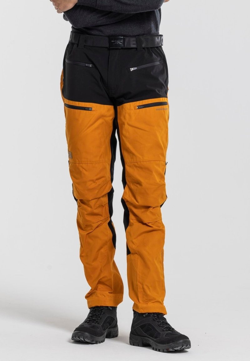 Orange und schwarze Outdoor-Hosen mit mehreren Reißverschlusstaschen, verstellbarem Gürtel und strukturiertem Stoff. Eigenschaften sind verstärkte Knie und schmal zulaufende Passform.
