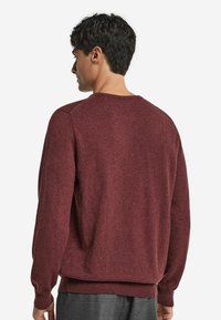 Bordeauxroter Pullover mit Rundhalsausschnitt, gerippten Ärmelbündchen und Saum, aus einem strukturierten Strickmaterial gefertigt. Das Design ist schlicht und klassisch.