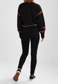 Czarna bluza z nadrukiem w czerwone i białe wzory, w połączeniu z czarnymi dopasowanymi dżinsami i czarnymi sneakersami z teksturowaną podeszwą.